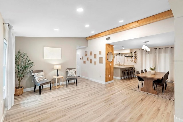 living area with light hardwood / wood-style floors, an inviting chandelier, lofted ceiling with beams, and sink