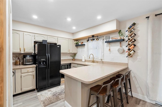 kitchen with sink, black fridge, light wood-type flooring, tasteful backsplash, and kitchen peninsula