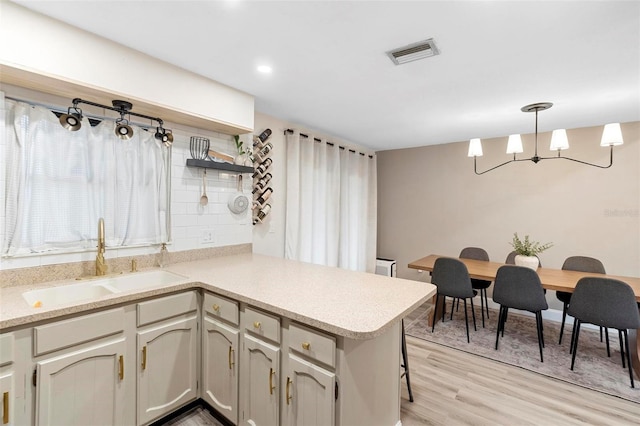 kitchen with kitchen peninsula, light hardwood / wood-style flooring, a wealth of natural light, hanging light fixtures, and sink