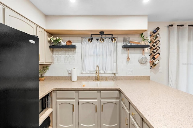 kitchen featuring decorative backsplash, black refrigerator, and sink