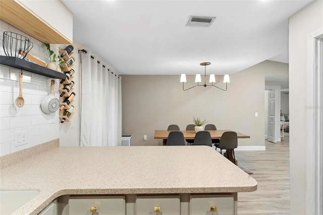 kitchen featuring an inviting chandelier, tasteful backsplash, hanging light fixtures, and light hardwood / wood-style flooring