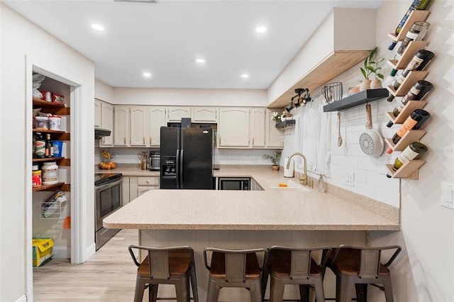 kitchen featuring black fridge with ice dispenser, sink, stainless steel electric range oven, kitchen peninsula, and a breakfast bar area