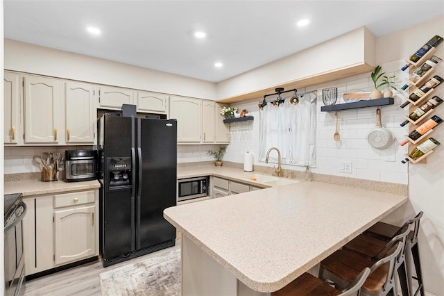 kitchen with black fridge with ice dispenser, range with electric cooktop, sink, and kitchen peninsula