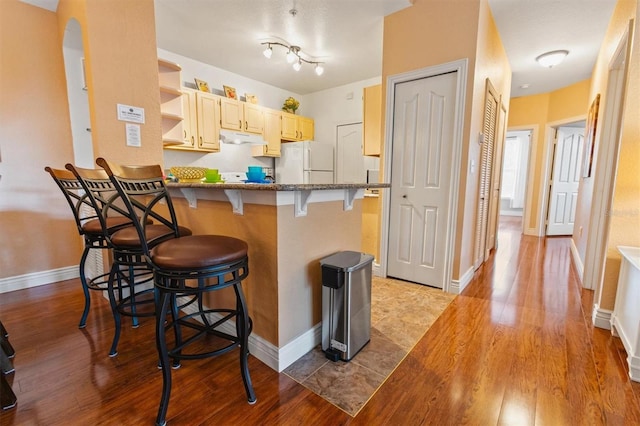 kitchen featuring a kitchen breakfast bar, light hardwood / wood-style floors, light brown cabinetry, white fridge, and kitchen peninsula