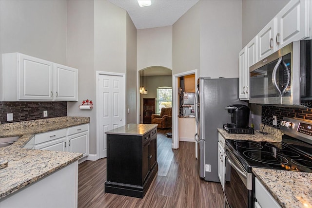 kitchen featuring light stone countertops, appliances with stainless steel finishes, a kitchen island, a high ceiling, and white cabinetry