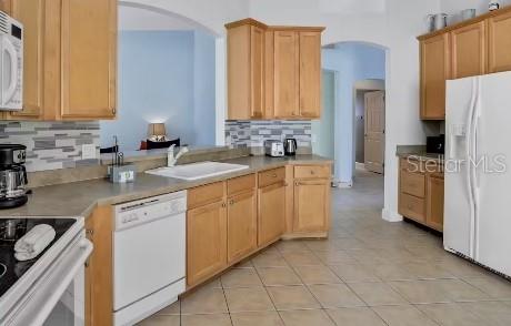 kitchen featuring decorative backsplash, light tile patterned floors, white appliances, and sink