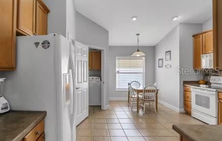 kitchen featuring light tile patterned flooring, pendant lighting, white appliances, and washer / dryer