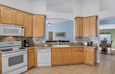 kitchen featuring tasteful backsplash, white appliances, ceiling fan, sink, and a high ceiling