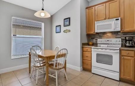 kitchen with white appliances, backsplash, hanging light fixtures, vaulted ceiling, and light tile patterned floors