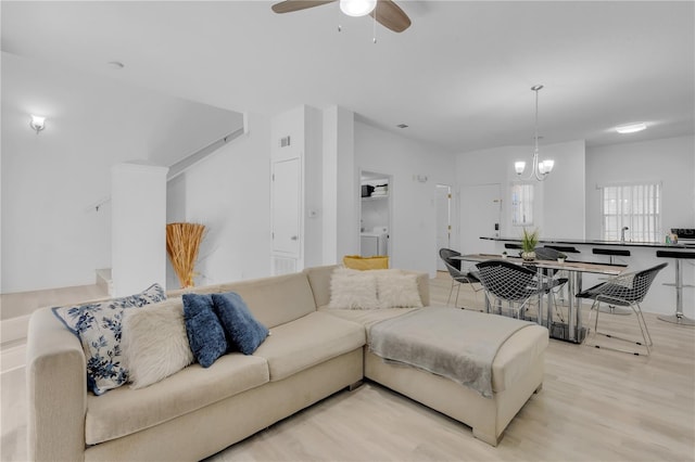 living room featuring ceiling fan with notable chandelier, washer / clothes dryer, and light hardwood / wood-style flooring