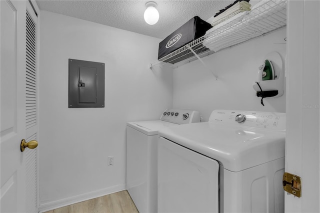 laundry room featuring separate washer and dryer, a textured ceiling, electric panel, and light hardwood / wood-style flooring