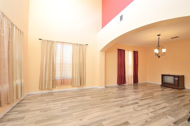 unfurnished living room with a chandelier, a high ceiling, and light hardwood / wood-style floors