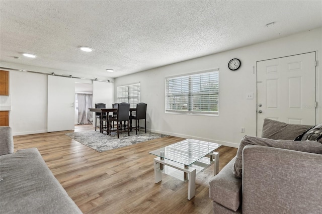 living room featuring a barn door, a textured ceiling, and light hardwood / wood-style flooring