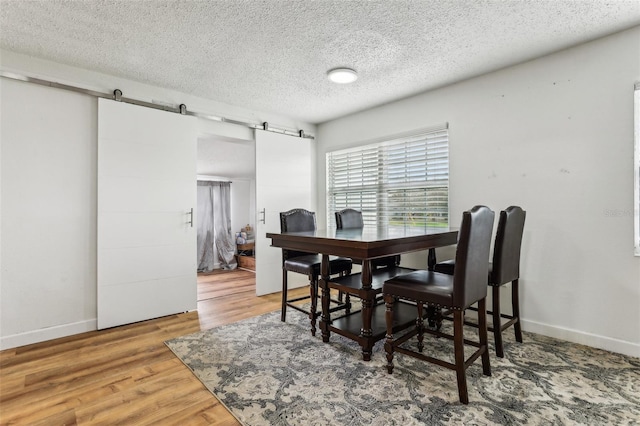 dining space with a barn door, wood-type flooring, and a textured ceiling