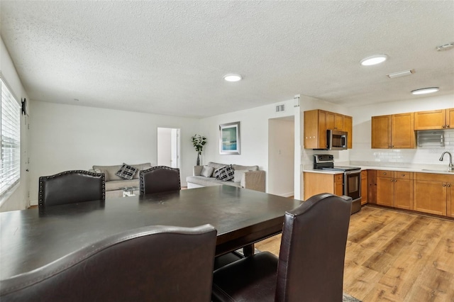 dining area with a textured ceiling, light wood-type flooring, and sink