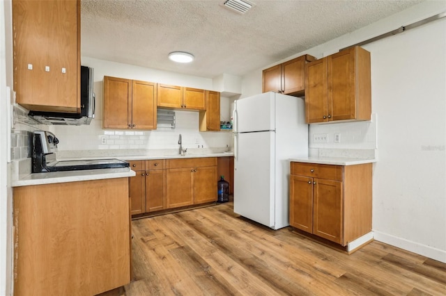 kitchen featuring sink, stove, white fridge, light hardwood / wood-style floors, and a textured ceiling