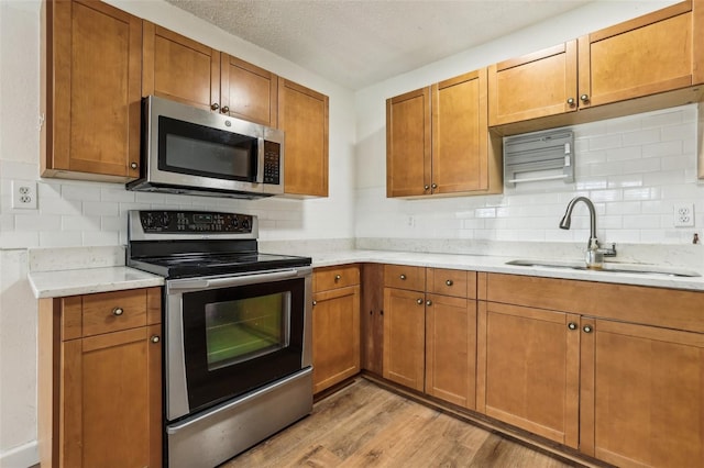 kitchen with backsplash, sink, a textured ceiling, light hardwood / wood-style floors, and stainless steel appliances