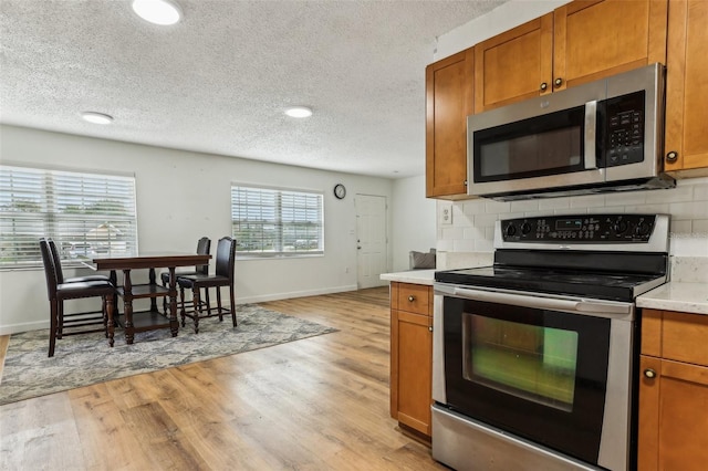 kitchen with a textured ceiling, light wood-type flooring, stainless steel appliances, and tasteful backsplash