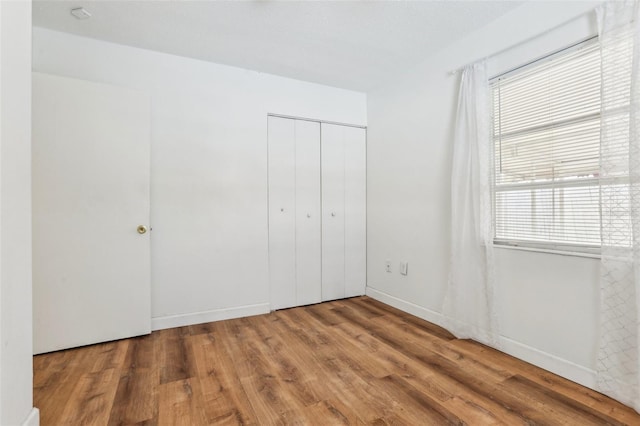 unfurnished bedroom featuring wood-type flooring, a closet, and multiple windows