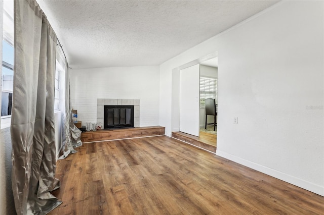 unfurnished living room featuring wood-type flooring, a textured ceiling, and a tiled fireplace