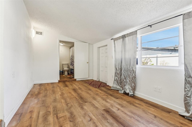 empty room featuring light hardwood / wood-style floors, a textured ceiling, and vaulted ceiling