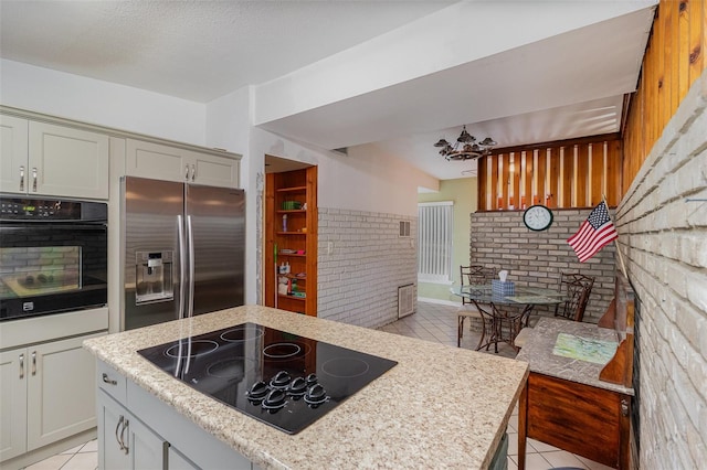 kitchen featuring brick wall, light tile patterned floors, a textured ceiling, and black appliances