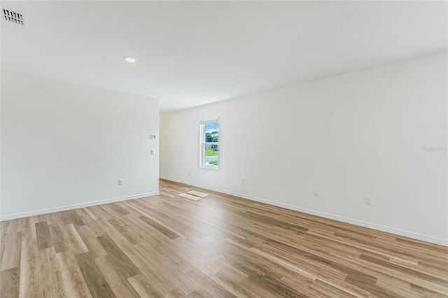 empty room with light wood-style flooring, visible vents, and baseboards