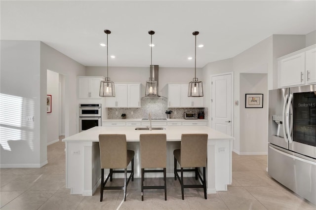 kitchen with white cabinetry, wall chimney exhaust hood, pendant lighting, a kitchen island with sink, and appliances with stainless steel finishes