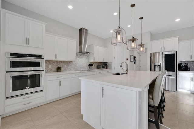 kitchen with pendant lighting, a kitchen island with sink, sink, wall chimney exhaust hood, and appliances with stainless steel finishes