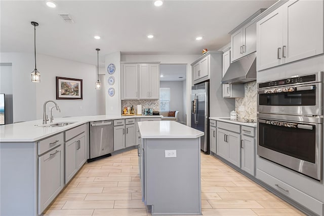 kitchen with decorative backsplash, stainless steel appliances, gray cabinets, hanging light fixtures, and an island with sink