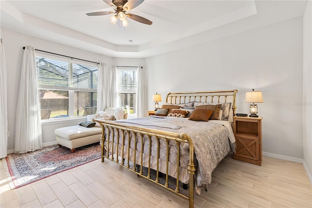 bedroom with ceiling fan, light wood-type flooring, and a tray ceiling