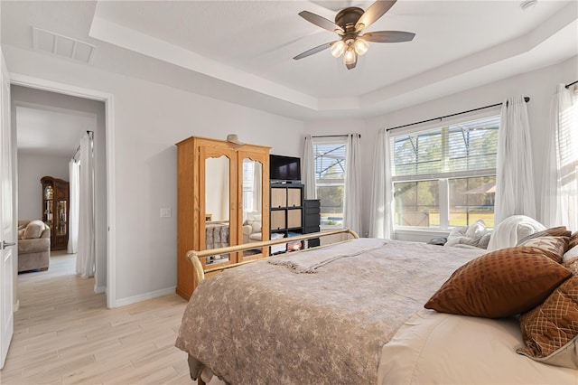 bedroom with light hardwood / wood-style floors, a raised ceiling, and ceiling fan