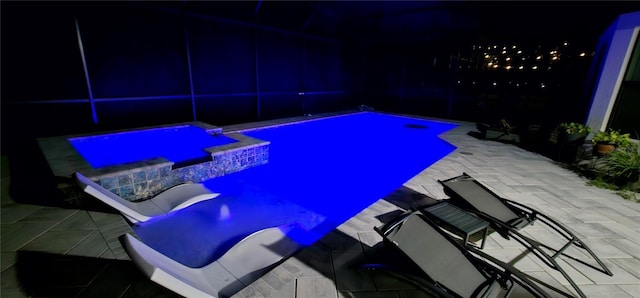 pool at night with an in ground hot tub and a patio area