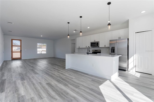 kitchen with stainless steel appliances, a kitchen island with sink, pendant lighting, white cabinets, and light hardwood / wood-style floors