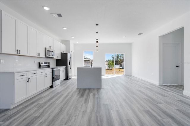 kitchen featuring appliances with stainless steel finishes, light wood-type flooring, white cabinetry, and pendant lighting