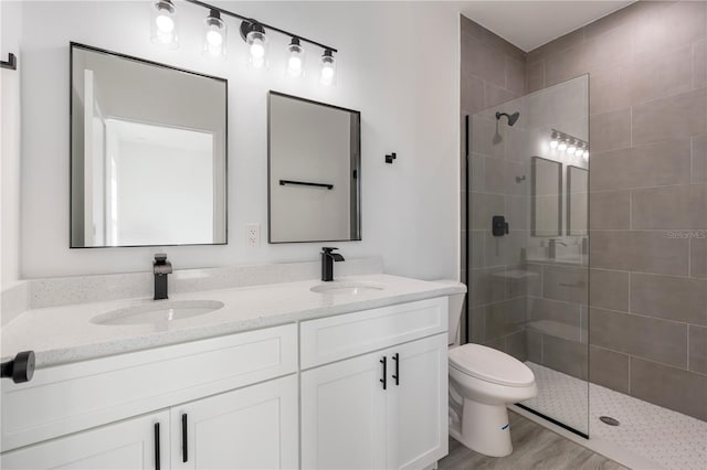 bathroom featuring hardwood / wood-style flooring, toilet, vanity, and tiled shower