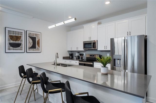 kitchen featuring white cabinetry, sink, hanging light fixtures, stainless steel appliances, and a kitchen bar