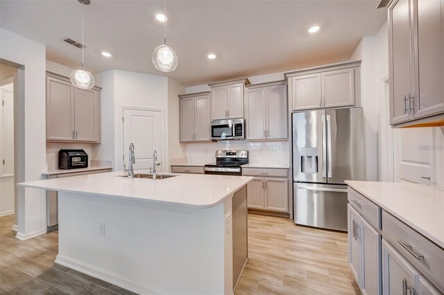 kitchen featuring stainless steel appliances, sink, decorative light fixtures, gray cabinets, and an island with sink