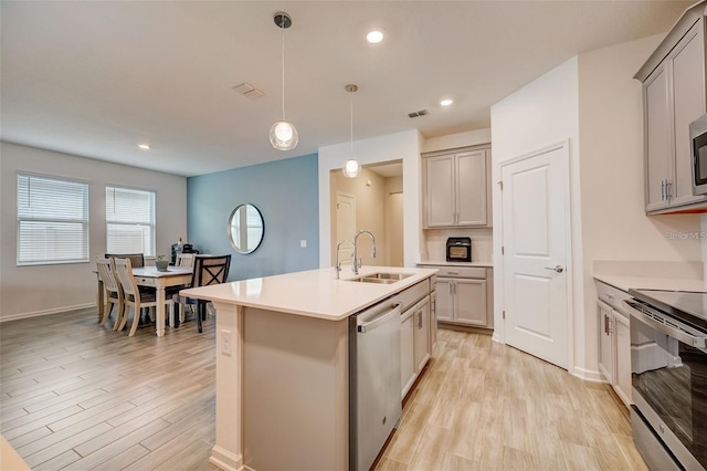 kitchen with sink, pendant lighting, light hardwood / wood-style floors, a kitchen island with sink, and appliances with stainless steel finishes