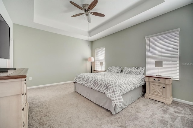 carpeted bedroom with ceiling fan and a tray ceiling