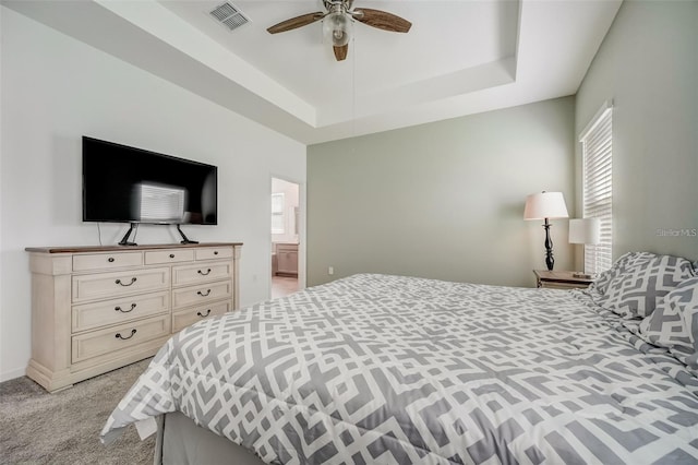 carpeted bedroom featuring ensuite bathroom, ceiling fan, and a raised ceiling