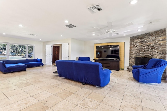 tiled living room with ceiling fan and a stone fireplace