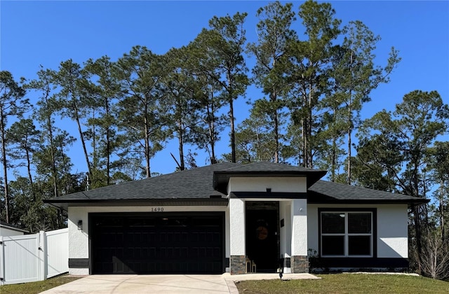 prairie-style home featuring an attached garage, driveway, stone siding, a gate, and stucco siding