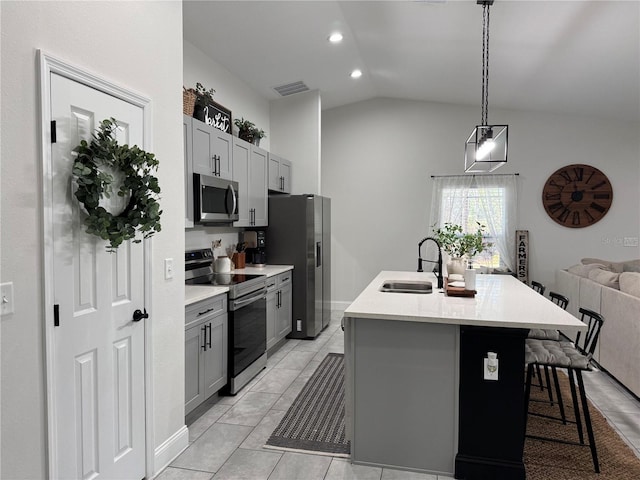 kitchen featuring appliances with stainless steel finishes, lofted ceiling, an island with sink, sink, and gray cabinetry