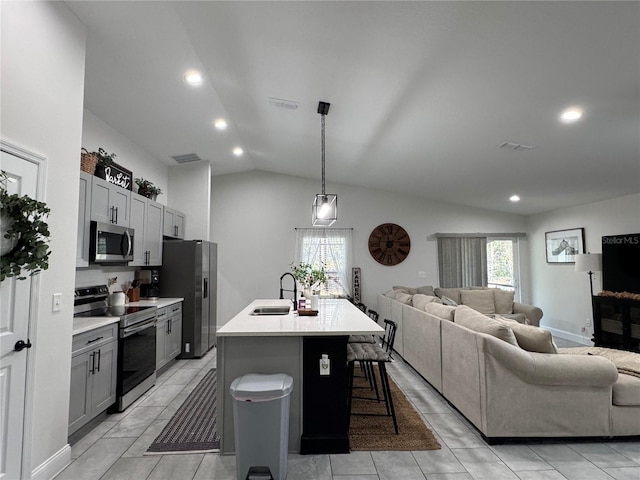 kitchen featuring appliances with stainless steel finishes, an island with sink, gray cabinets, vaulted ceiling, and a breakfast bar area