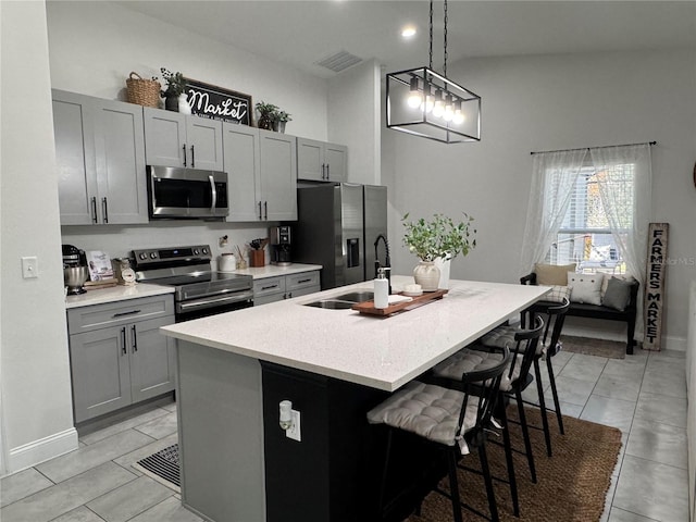 kitchen featuring decorative light fixtures, appliances with stainless steel finishes, gray cabinetry, and an island with sink