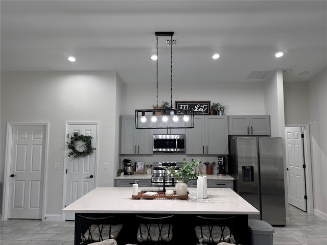 kitchen with decorative light fixtures, gray cabinets, stainless steel appliances, and a kitchen island with sink