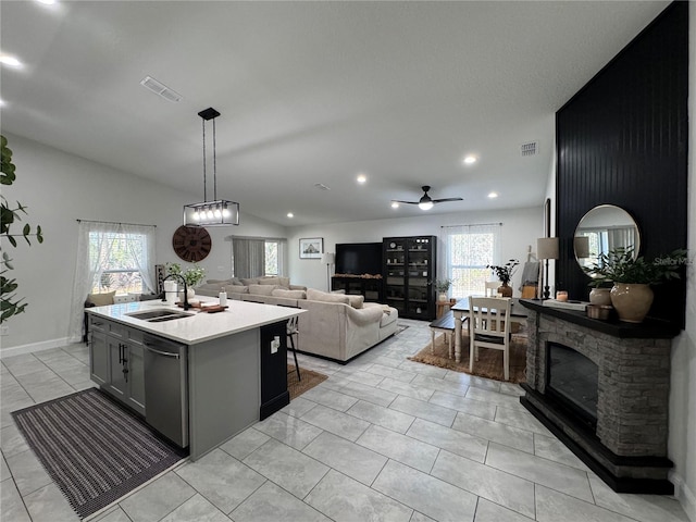 kitchen with vaulted ceiling, pendant lighting, stainless steel dishwasher, sink, and an island with sink