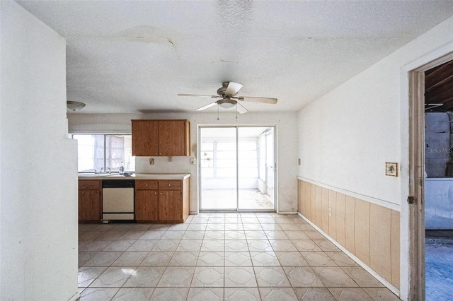 kitchen with stainless steel dishwasher, ceiling fan, a textured ceiling, and wooden walls