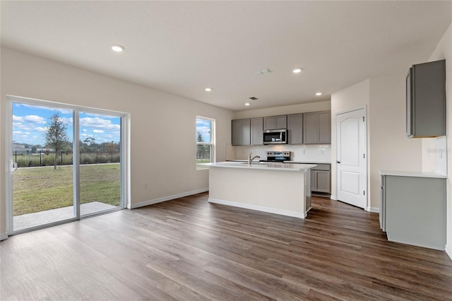 kitchen featuring appliances with stainless steel finishes, dark hardwood / wood-style flooring, a wealth of natural light, gray cabinets, and an island with sink